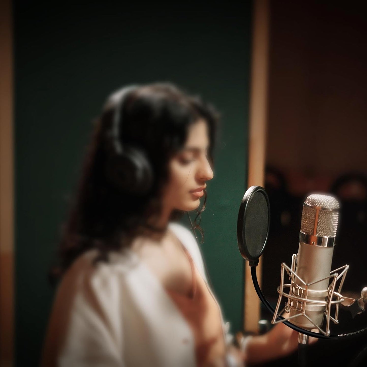 Content creator in a Kenyan recording studio using a studio microphone pop filter to reduce plosive sounds during vocal recording.