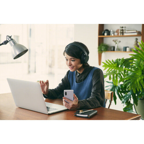 Woman wearing Sony WH-CH720N Kenya headphones on a video call at a desk with laptop and phone