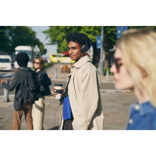 Man wearing Sony WH-CH720N Kenya headphones outdoors on a busy street, holding a coffee cup