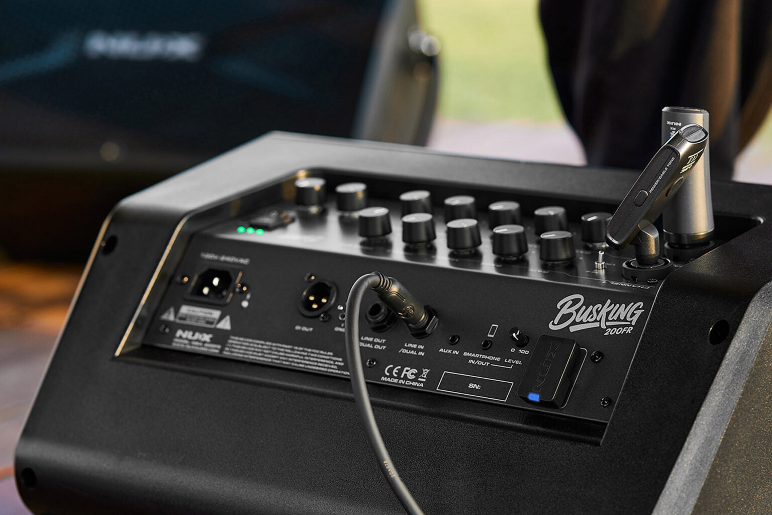 NUX Busking 200FR PA Kenya in outdoor use with XLR cable connected, green LEDs and wireless mic on top