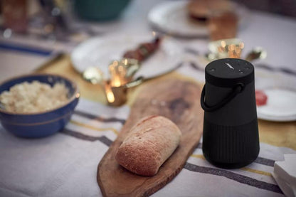 Bose SoundLink Revolve+ II Kenya placed on a dining table in a warm indoor setting with candles