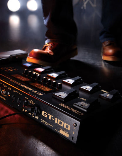 Boss GT-100 Kenya on stage floor with performer's foot pressing footswitch under stage lighting